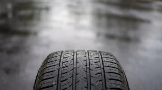 Gros plan artistique sur la bande de roulement d'un pneu sous une pluie fine, symbolisant la sécurité routière et l'usure des pneumatiques