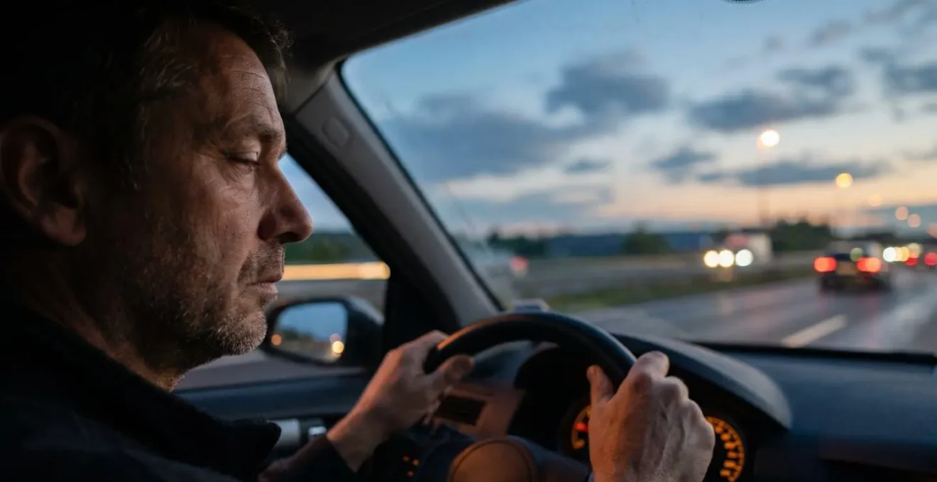 Conducteur aux paupières lourdes au volant d'une voiture au crépuscule sur une route d'autoroute, illustrant les signaux d'alerte de la fatigue au volant