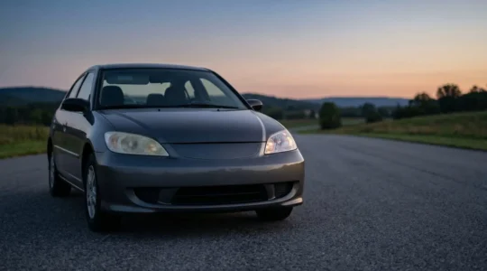 Gros plan sur un phare de voiture dont une partie est opaque et jaunie tandis que l'autre est redevenue transparente, sur une route au crépuscule