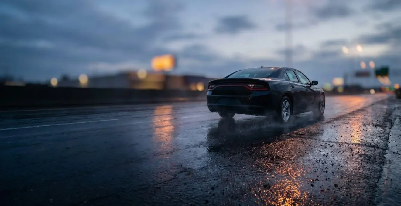 Voiture roulant prudemment sur une route mouillée la nuit, avec des reflets de lumière sur l'asphalte illustrant le risque de perte de controle